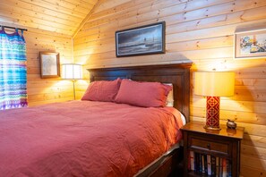 A wooden cabin bedroom with a bed, two bedside lamps, a framed picture, and a small bookshelf. - Cabin 2 at Widows Peak • Terlingua, Big Bend (Terlingua)
