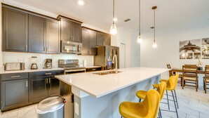 Una cucina moderna con pensili scuri, elettrodomestici in acciaio inossidabile, una grande isola con sgabelli da bar e illuminazione a sospensione.