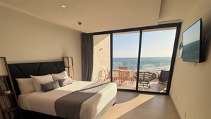Ein modernes Hotelzimmer mit einem großen Bett, einem Balkon mit Meerblick und einem an der Wand befestigten Flachbildfernseher.