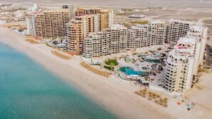 Ein Hotelkomplex an der Küste mit mehreren Hochhäusern, direkt am Strand und einem zentralen Poolbereich.