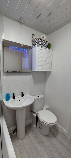 A bathroom with a white sink, toilet, and bathtub. There is a mirror above the sink and a ceiling light fixture. - Paisley Pattern Flat West End UWS UNI GLA Glasgow Airport (Paisley)