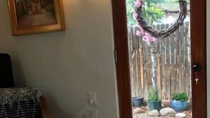 Huone, jossa on puinen ovi, rottinkituoli, seinällä oleva kehystetty kuva ja ovimatto.