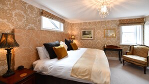 A bedroom with a large bed, two bedside tables, a chair, a chandelier, and a window with a view. - The Townhouse (Ayr)