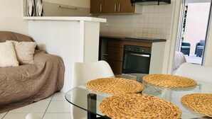 Una sala moderna con una mesa de comedor de cristal, sillas blancas y un sofá beige.