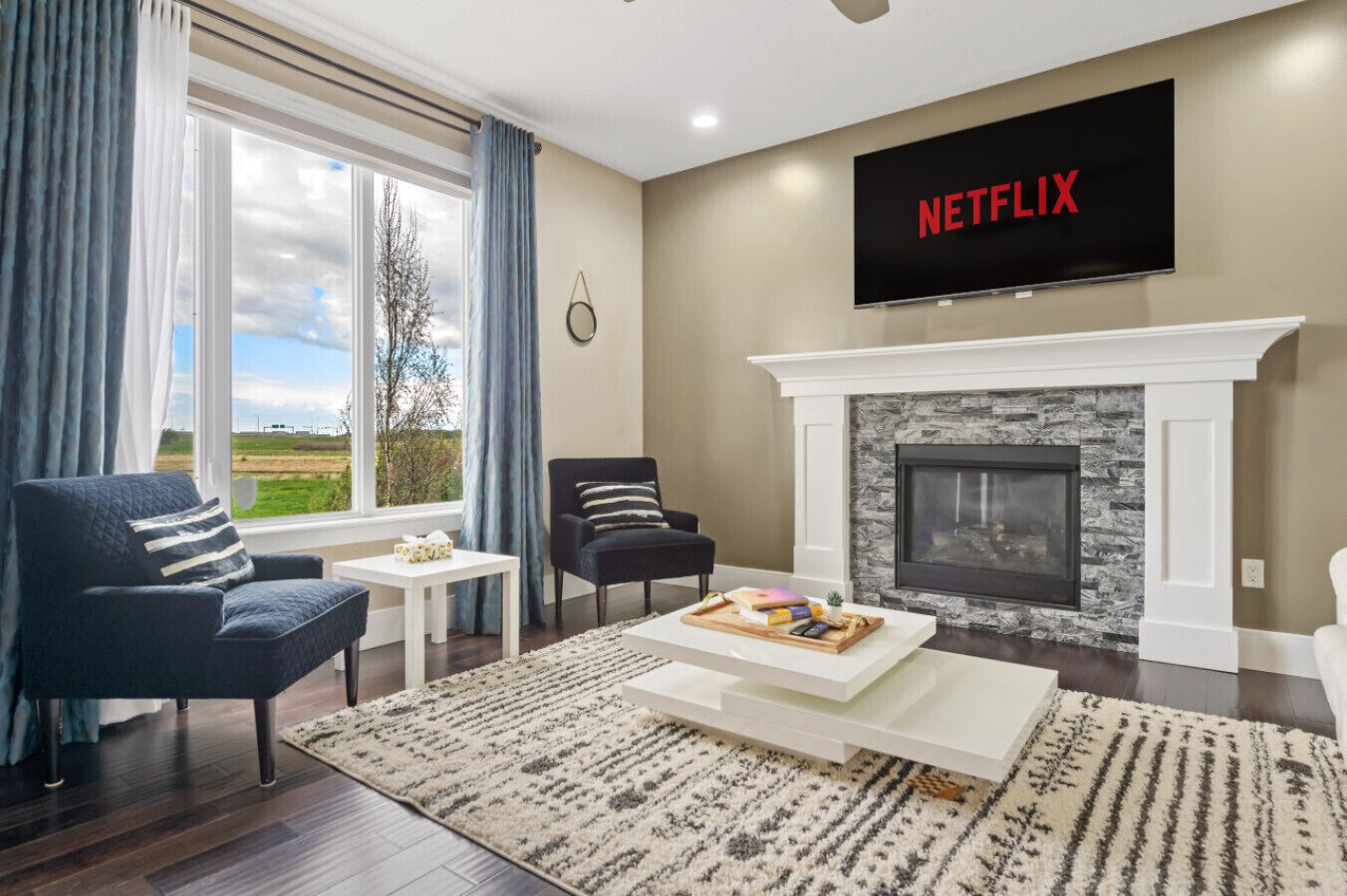 Uma sala de estar com lareira, uma TV montada acima e vista para o exterior por grandes janelas.