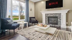 Ein Wohnzimmer mit Kamin, einem darüber montierten Fernseher und Blick ins Freie durch große Fenster.