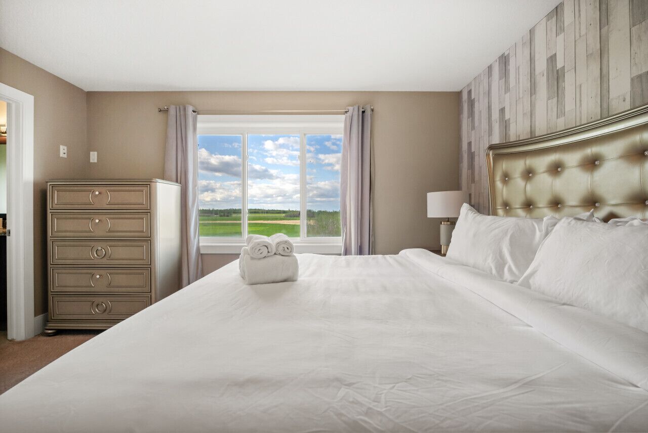 Quarto de hotel com uma cama grande, cômoda e janela com vista para o campo.
