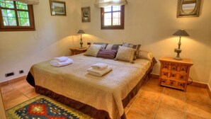 A bedroom with a large bed, two bedside tables with lamps, a rug, and two windows with curtains.