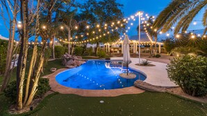 Una piscina circondata da alberi e luci decorative, con una zona salotto coperta sullo sfondo.