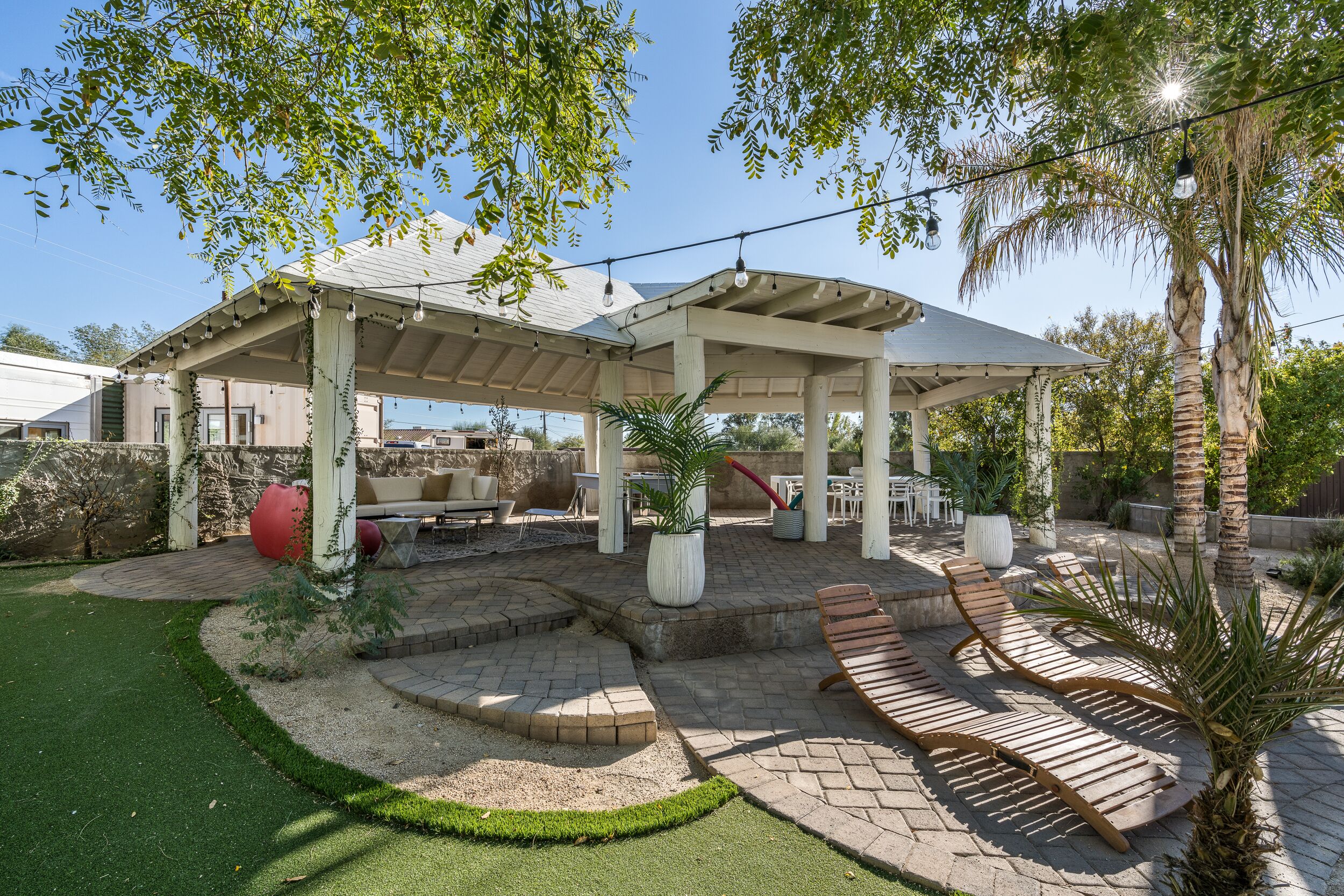 A covered patio area with outdoor seating, a fire pit, and a well-maintained lawn.