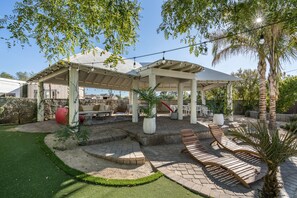 A covered patio area with outdoor seating, a fire pit, and a well-maintained lawn.