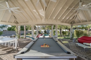 An outdoor pool table under a covered area with a view of a backyard.