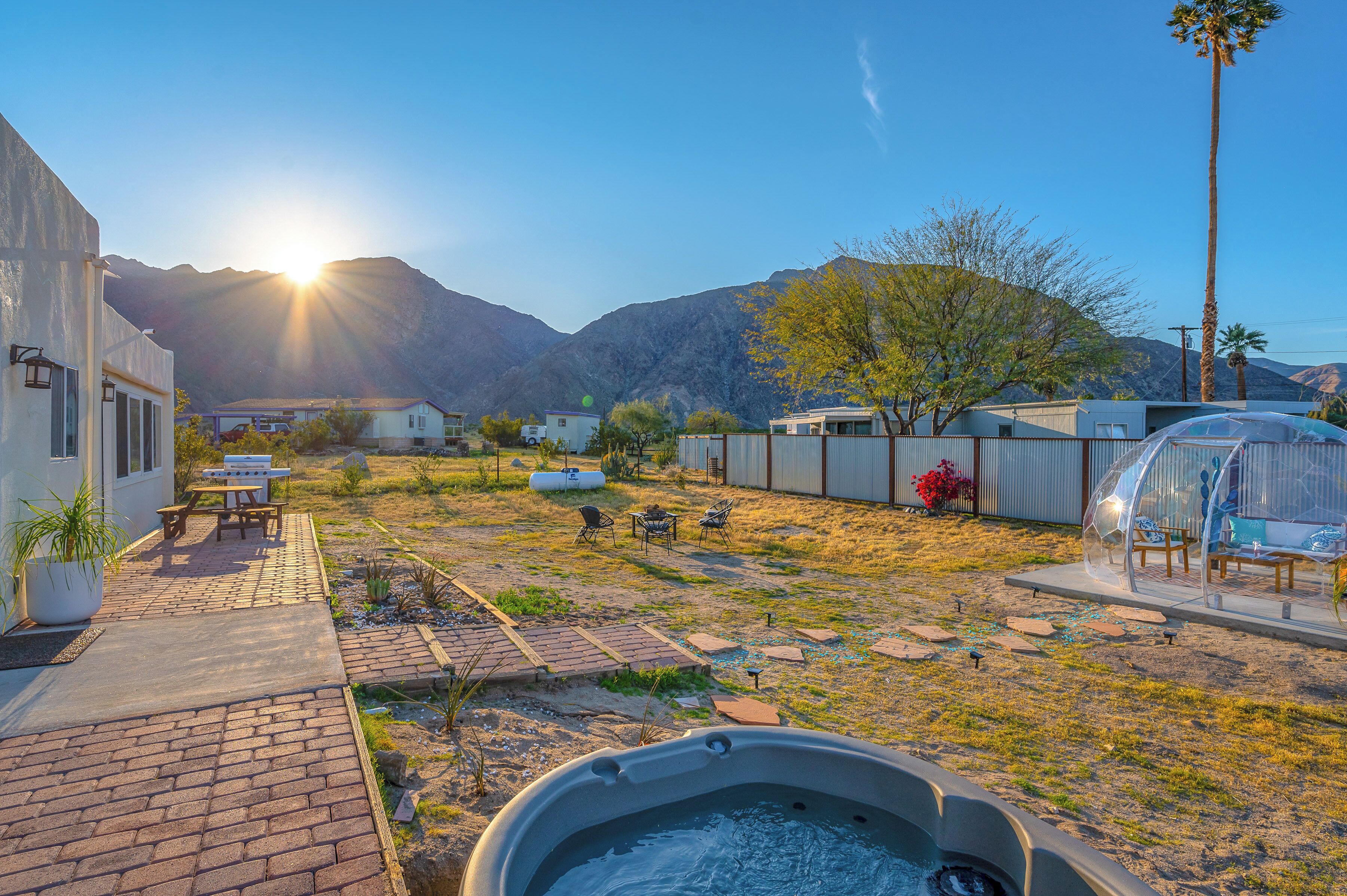 Un jardin avec un jacuzzi, des meubles de patio et une vue sur les montagnes en arrière-plan.