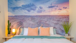 Un dormitorio con un mural grande de un cañón, una cama con varias almohadas, una lámpara de noche y una planta en maceta.