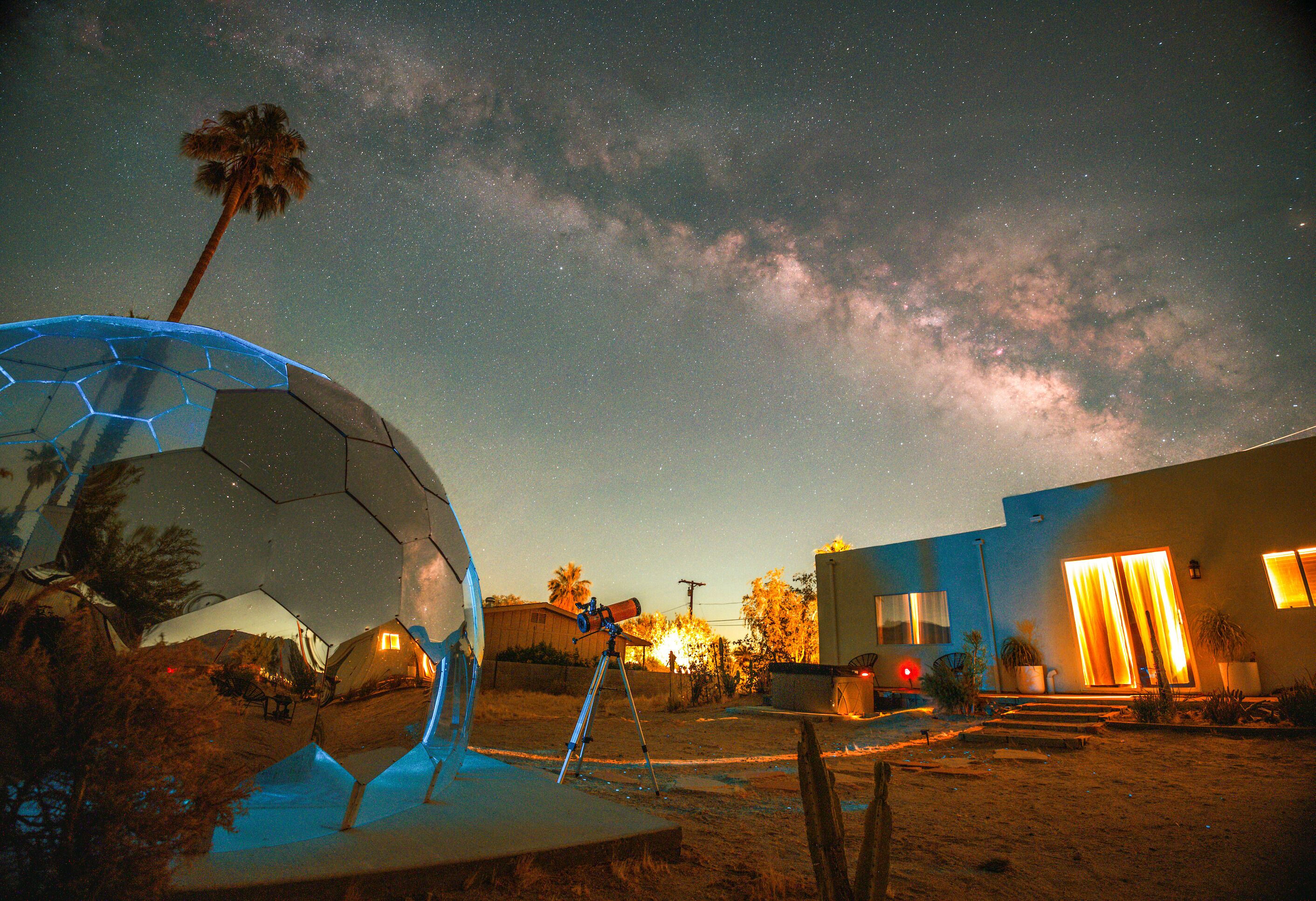 Un cielo stellato con un telescopio e una struttura a cupola geodetica.