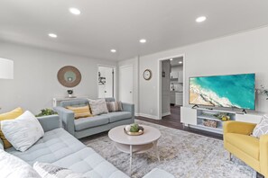 A modern living room with a grey sofa, a yellow armchair, a coffee table, and a TV displaying a beach scene. - Gather the Fam! Close to everything, Home Theater, 2 Kitchens, 2 Living Rooms! (Wisconsin Dells)