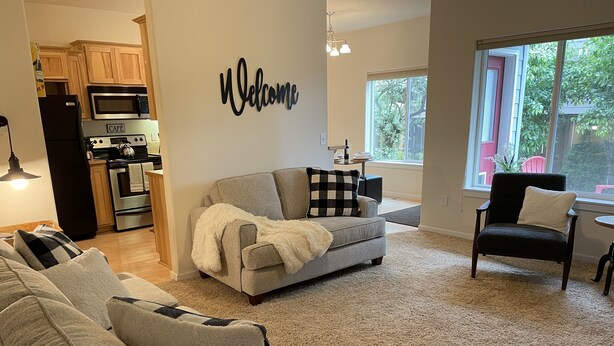 A modern living room with a grey sofa, a black armchair, and a 'Welcome' sign on the wall. - Pacific University Stay,  very close to the University and downtown Forest Grove (Forest Grove)