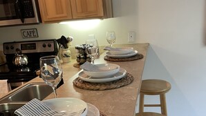 A kitchen with a long countertop, wooden cabinets, and a stove labeled "CAFE". There are three sets of plates and glasses on woven placemats, and a striped napkin is folded on one plate. - Pacific University Stay,  very close to the University and downtown Forest Grove (Forest Grove)