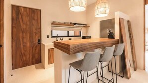 A modern kitchen with a wooden island, bar stools, pendant lighting, and a large mirror. - Balam Bohemian Paradise Beach Club + Private Pool (Tulum)