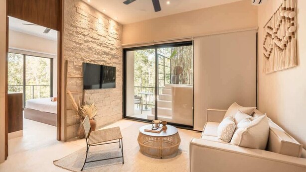A modern living room with a stone wall, a flat-screen TV, a sofa, a round coffee table, and a ceiling fan. - Balam Bohemian Paradise Beach Club + Private Pool (Tulum)
