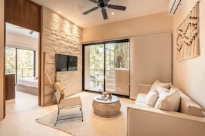 A modern living room with a stone wall, a flat-screen TV, a sofa, a round coffee table, and a ceiling fan.