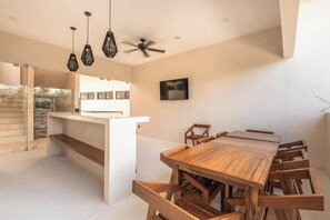 A modern dining area with a wooden table and chairs, a ceiling fan, pendant lights, and a TV on the wall. - Balam Bohemian Paradise Beach Club + Private Pool (Tulum)