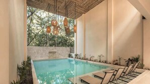 A pool area with lounge chairs, a stone wall, and hanging lights. - Balam Bohemian Paradise Beach Club + Private Pool (Tulum)