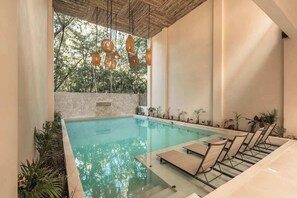 A pool area with lounge chairs, a stone wall, and hanging lights. - Balam Bohemian Paradise Beach Club + Private Pool (Tulum)