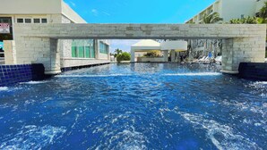 A swimming pool with a stone bridge overhead, surrounded by buildings. - Seaside Escape renovated Studio at turquoise Cancun beach  (Cancún)