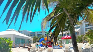 A resort pool area with lounge chairs, a water play structure, and palm trees. - Seaside Escape renovated Studio at turquoise Cancun beach  (Cancún)