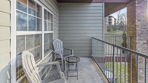 Un balcón con dos sillas Adirondack y una mesita, con vista a un área verde y edificios vecinos.