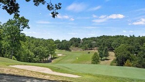 Un campo de golf con cielo despejado, árboles y una bandera en el green.