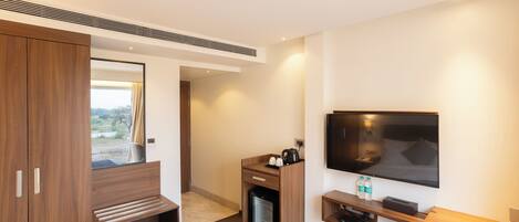 A modern hotel room with a bed, a TV, a mini-fridge, a desk, and a wardrobe.