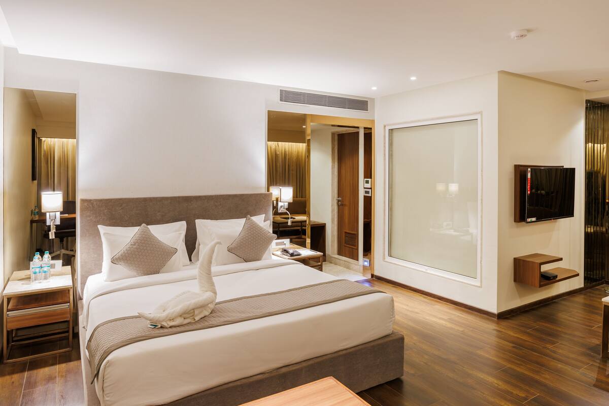 A hotel room with a large bed, bedside tables, a TV, and a door leading to a bathroom.