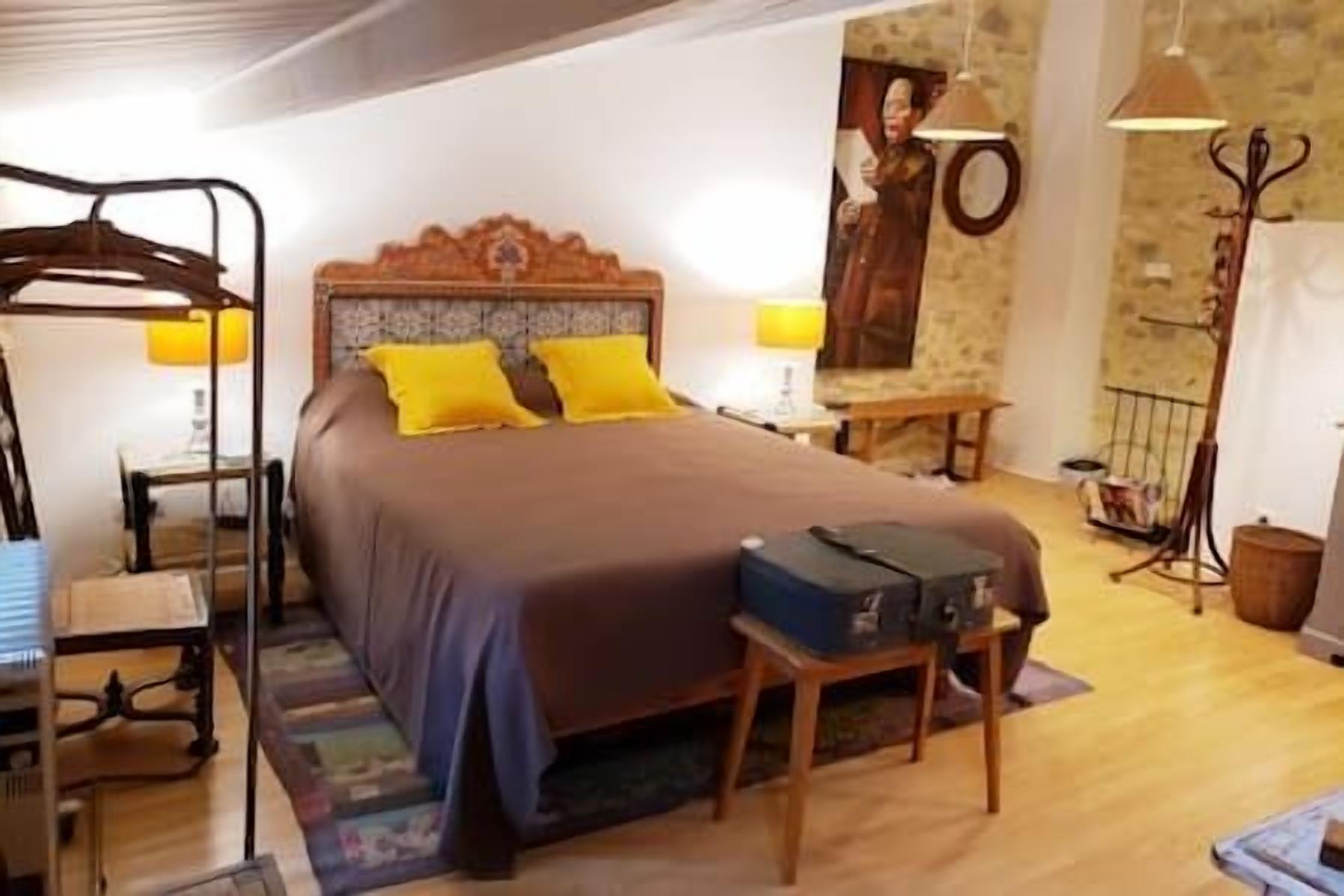 Ein Schlafzimmer mit einem großen Bett, zwei gelben Kissen, einem Holzkopfende, einem Nachttisch mit Lampe, einem Koffer auf einem kleinen Tisch und einer Steinwand mit einem gerahmten Bild.