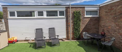 A backyard with artificial grass, two metal chairs, a table, and a red decorative item.