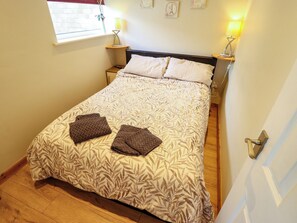 A neatly made bed with a leaf-patterned bedspread, two pillows, and two folded blankets on the floor. - Seaside Retreat (Skegness)