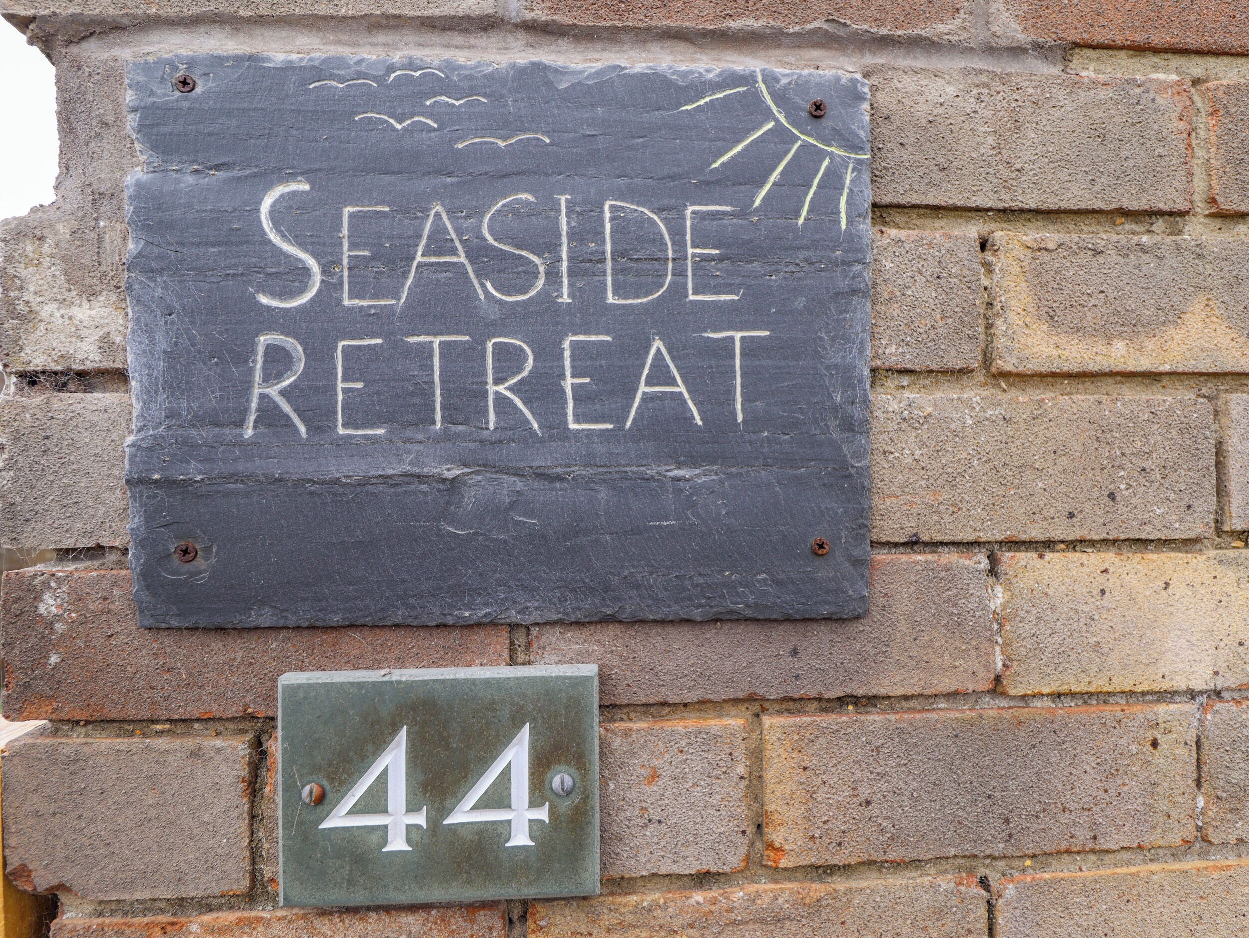 A sign for 'Seaside Retreat' with a number '44' below it, mounted on a brick wall.