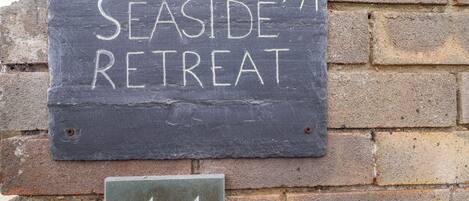 A sign for 'Seaside Retreat' with a number '44' below it, mounted on a brick wall.