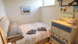 Um quarto com uma cama, cômoda, janela e prateleira fixada na parede.
