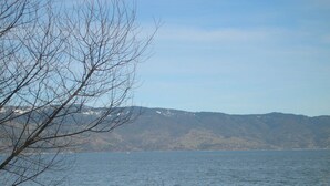 A calm lake with mountains in the background and leafless trees in the foreground. - Rainbow Lodge (Lakeport)