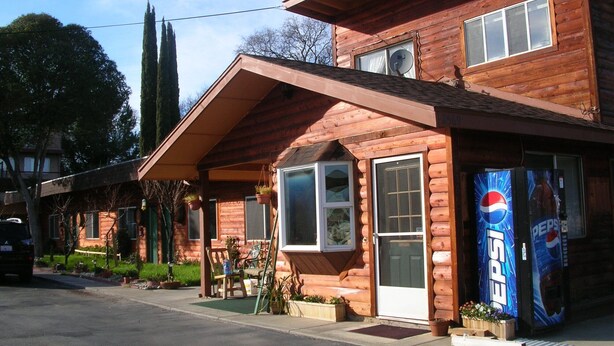 A wooden log cabin with a front porch, a Pepsi vending machine, and a car parked in front. - Rainbow Lodge (Lakeport)
