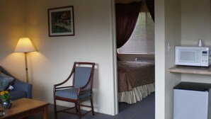 A hotel room with a bed, a chair, a lamp, a microwave, and a small refrigerator. - Rainbow Lodge (Lakeport)