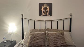 A bed with a metal headboard, two patterned pillows, a wall-mounted Buddha artwork, a bedside lamp, and a water bottle on a nightstand.