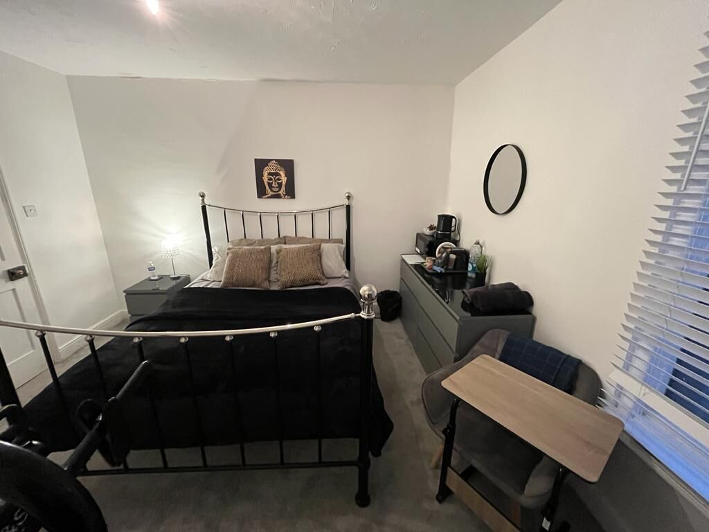 A bedroom with a bed, a desk, a chair, a mirror, and a Buddha statue.