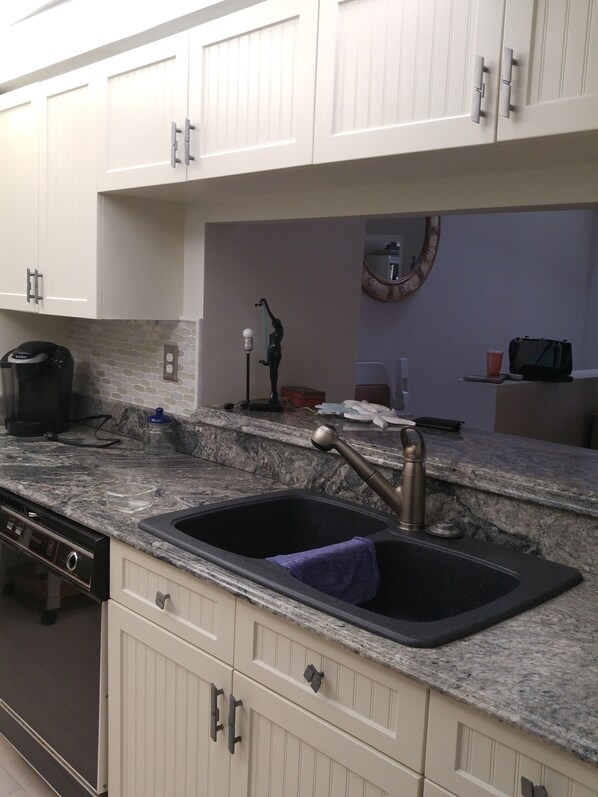 A kitchen with white cabinets, a granite countertop, a double sink, a coffee maker, and a small decorative item on the counter.