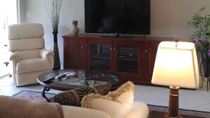 Een woonkamer met een bank, fauteuil, televisie, houten kast en een lamp.