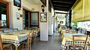 A restaurant with multiple tables and chairs, a tiled floor, and a view of the outside. - Calajunco1985 Sardinia Travel Experience (Loiri Porto San Paolo)