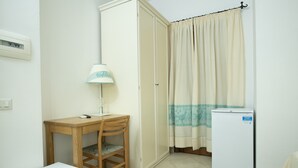 A small room with a wooden desk, a chair, a white cabinet, a white refrigerator, a curtain, and a wall-mounted light fixture. - Calajunco1985 Sardinia Travel Experience (Loiri Porto San Paolo)