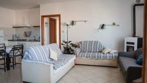 Un espacio habitable compacto con kitchenette, dos sofás, una mesa de comedor y un televisor pequeño.